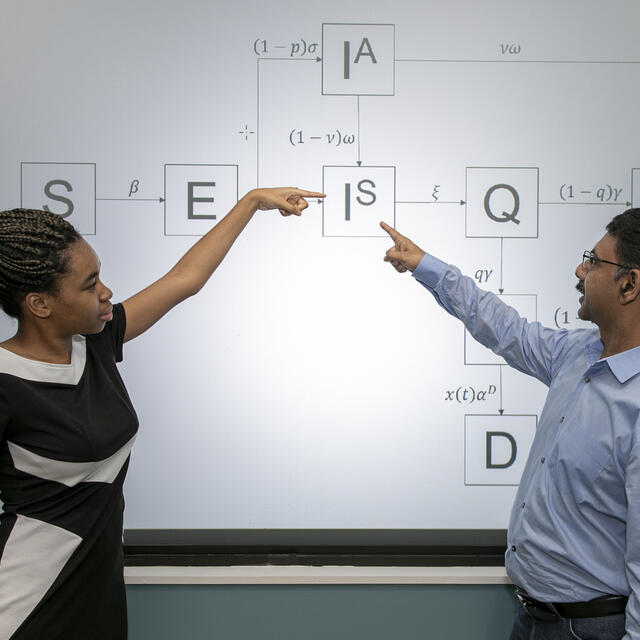 Student and professor pointing at screen with periodic table