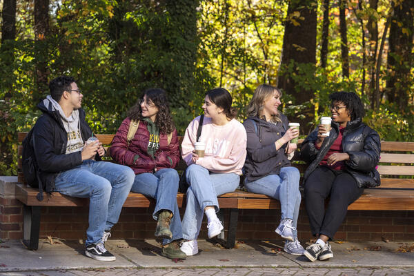 group of 5 students sitting on a bench and chatting 