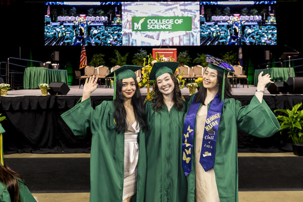3 students smiling, wearing their caps and gowns at graduation
