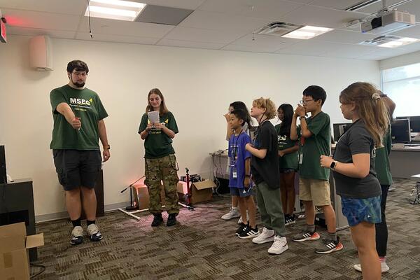 Several campers are assigning Ian instructions to write on the board. He appears to be struggling due to poor programming.