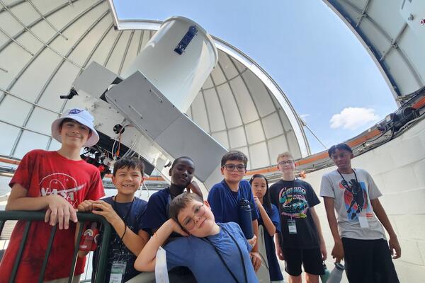 Many students are gathered the Geller Telscope. It is a sunny day as seen through the gap in the dome.