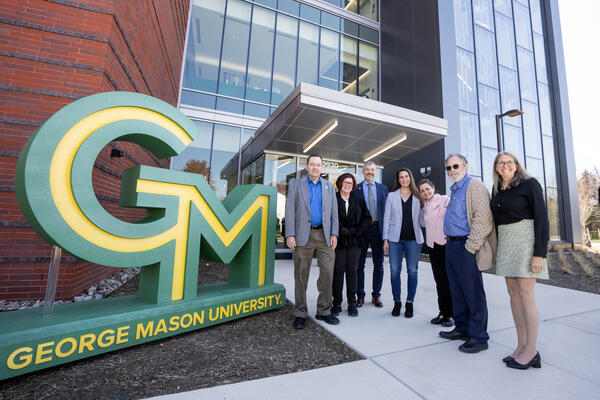 Group of faculty and staff in front of new George Mason logo at the new LSEB building on SciTech