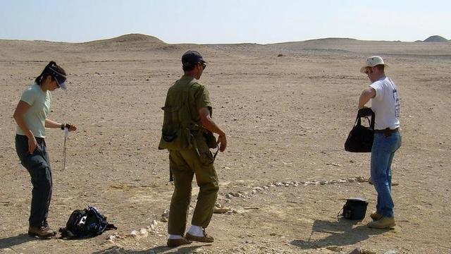 Scientists with whale fossil in desert.