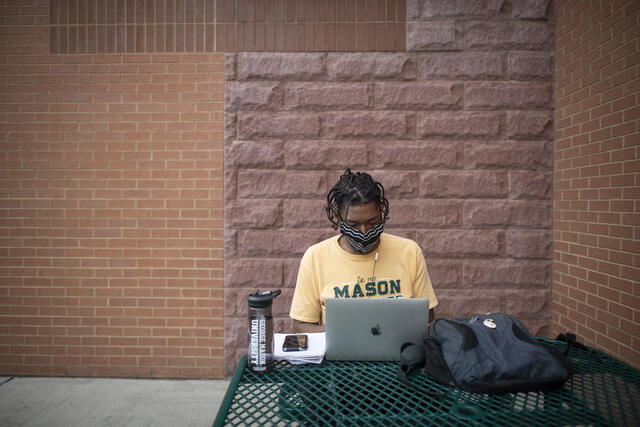 Mason student wearing face mask working on laptop