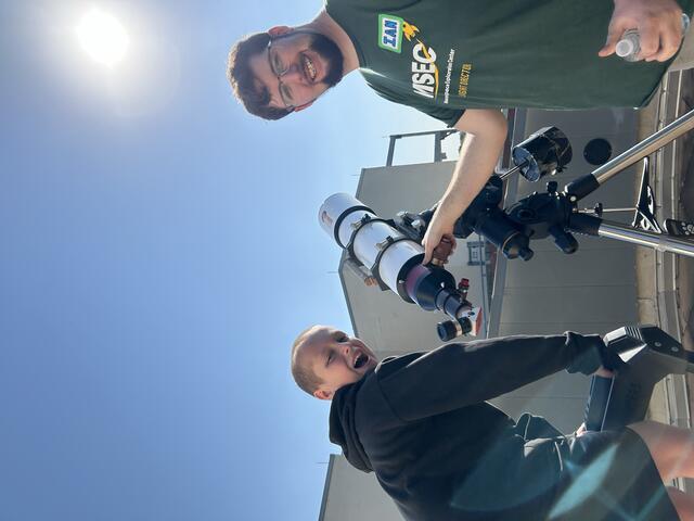 A Counselor and Camper are observing the Sun to spot the spots causing the recent aurora sightings. The camper has turned to the camera with a surpised look.