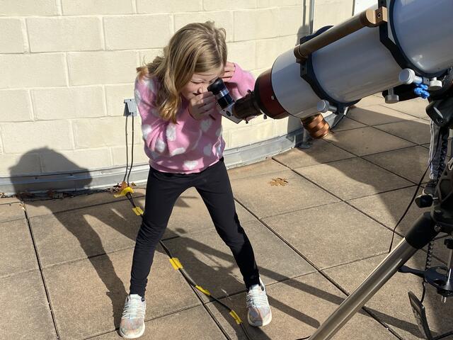 A camper observes the Sun through the filtered Lund telescope. Her shadow and the telescope's are cast upon the wall of the observatory.