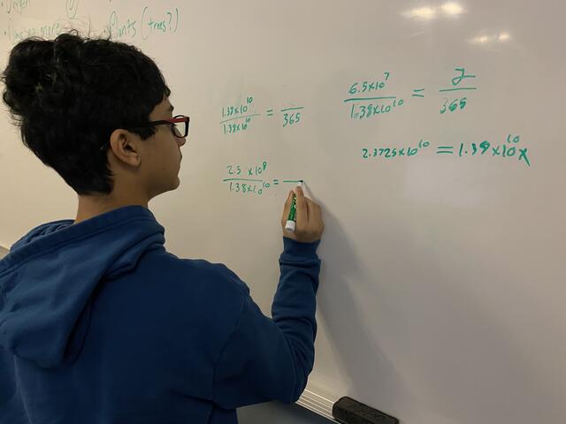 A camper performs a series of calculations on a whiteboard.