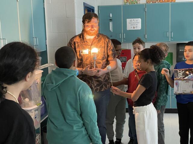 A crew member holds a lamp, while two students hold styrofoam balls on sticks to recreate the positions of the phases of the moon.