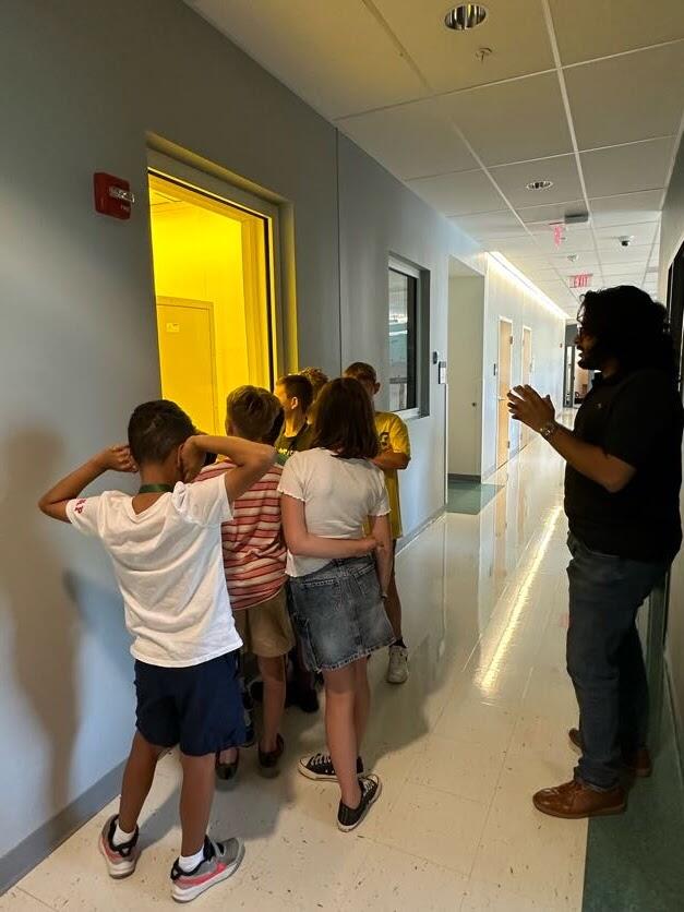 Campers are gathered around a glowing window as a College of Engineering graduate student explains what's inside.