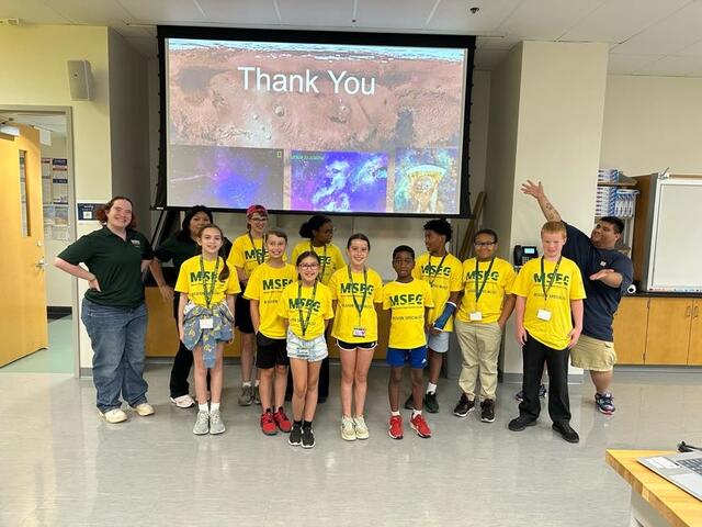 Campers line up for a group photo, posing in their George Mason Gold Shirts with Lead Flight Director Sebastian and his crew.