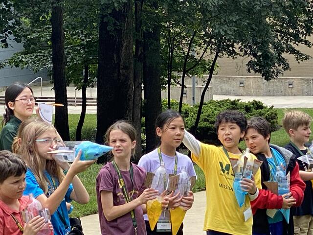 Campers react to water rocket launches. One appears to be drinking the fuel out of her rocket.