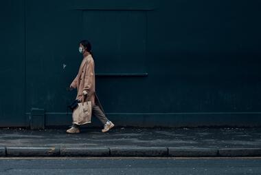 Woman in a mask walking down a street. Photo by Ross Sneddon on Unsplash.