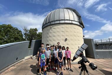A group of students are gathered on the roof on a sunny day in front of the Observatory Dome and our Solar Telescope.